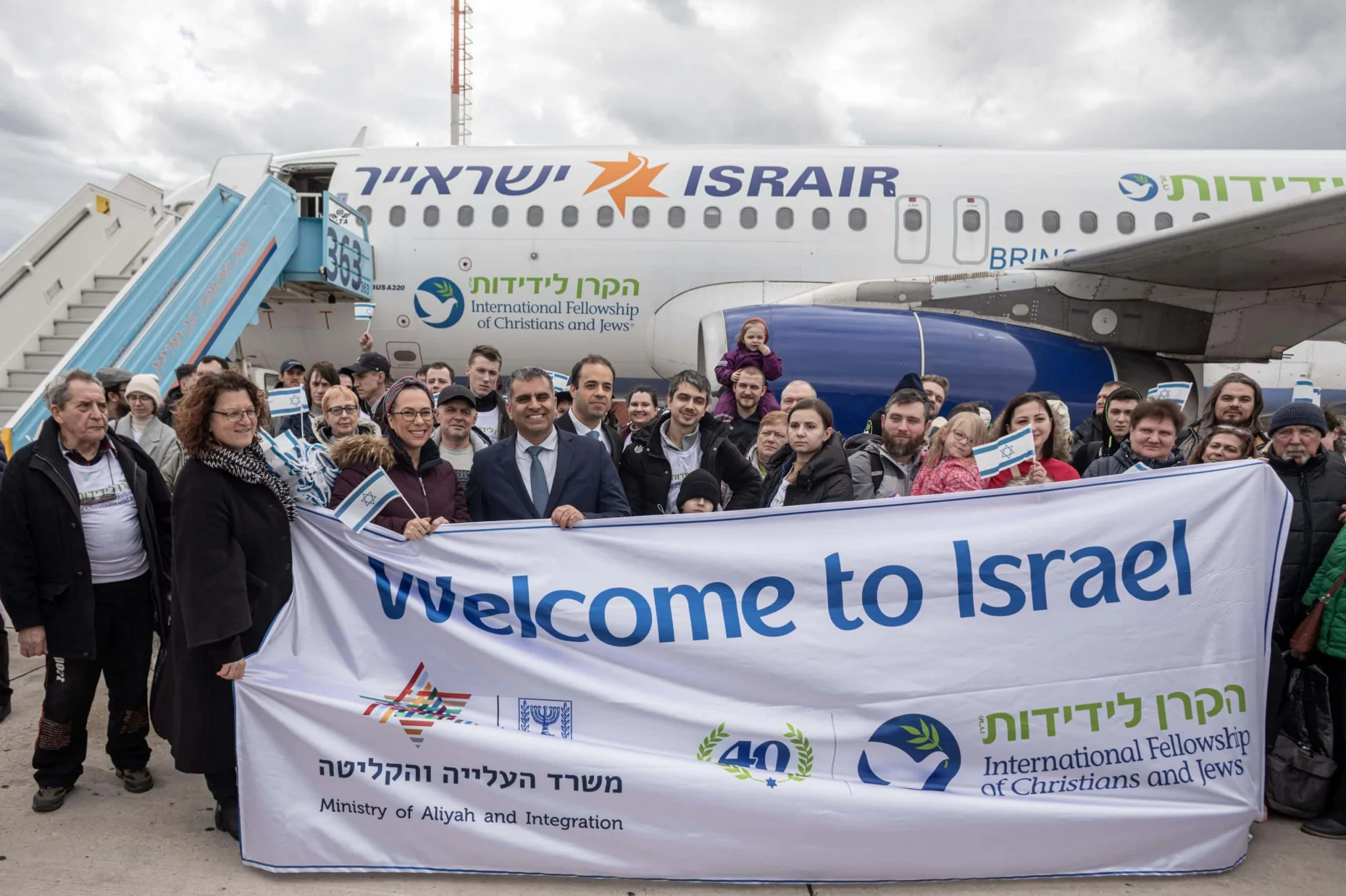 Groupe de nouveaux immigrants accueillis en Israël devant un avion d’Israir portant le logo de la Keren Layedidout.